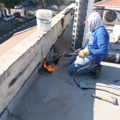 אדם משתמש במבער לאיטום גג עם יריעות ביטומניות.