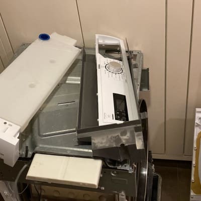 חלקי מכונת כביסה מפורקים, כולל לוח בקרה ומיכל פלסטיק