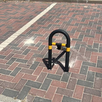 מחסום חניה מתכת שחור עם פס צהוב על אבנים משתלבות