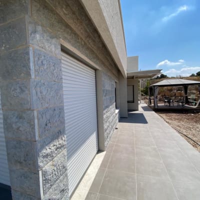 קיר אבן עם תריסים סגורים ומרפסת מרוצפת