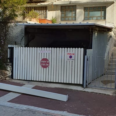 גג מתכת שטוח מעל חניה עם גדר עץ לבנה