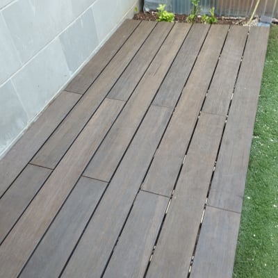 רצפת עץ חומה ליד קיר אבן וצמחים קטנים