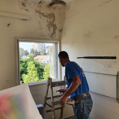 אדם צובע קיר עם סולם וחומרי צביעה