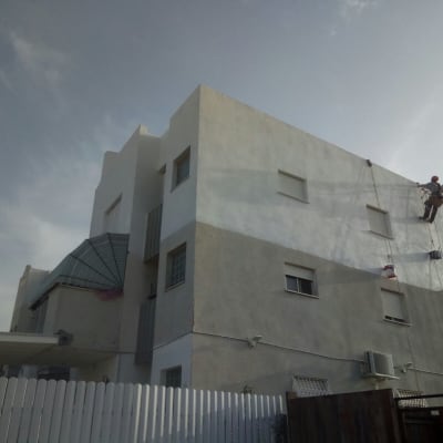 אדם צובע קיר חיצוני של בניין בעזרת חבלים