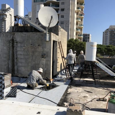 עובדים אוטמים גג עם יריעות ביטומניות וכלים