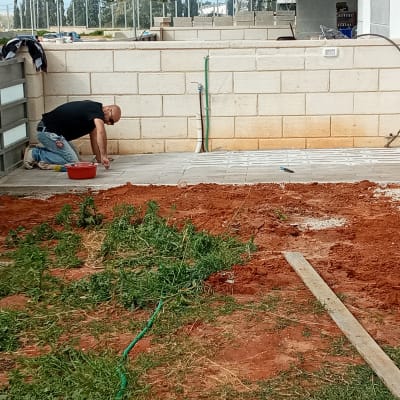 אדם עובד על ריצוף חצר עם כלים ודלי