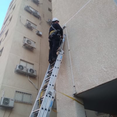 חשמלאי על סולם מתקין כבלים על קיר חיצוני