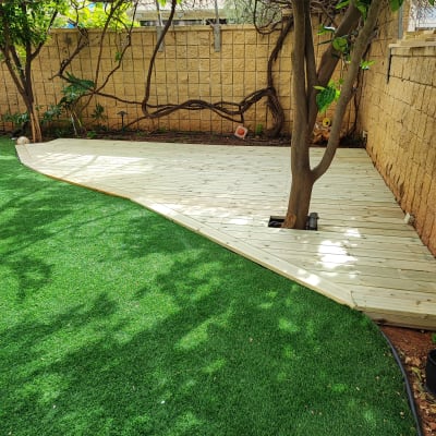 דק עץ ליד עץ בגינה עם דשא סינתטי