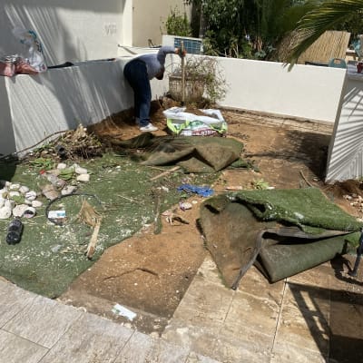 אדם מסיר דשא סינתטי בגינה עם כלי עבודה