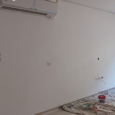 קיר צבוע לבן עם פחיות צבע ומברשת על הרצפה