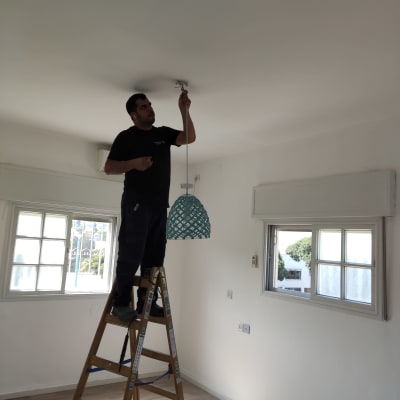 חשמלאי מתקין מנורה מהתקרה בעזרת סולם