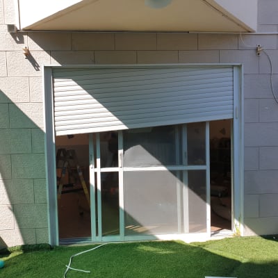 תריס גלילה לבן פתוח חלקית על חלון זכוכית