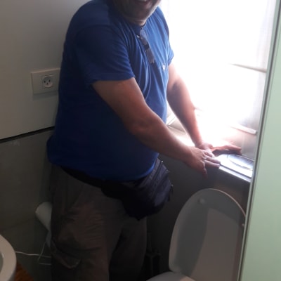 אדם ליד אסלה, לובש כובע ועובד בחדר אמבטיה