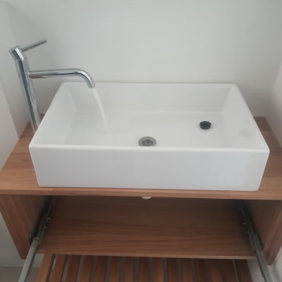 כיור לבן עם ברז מים זורמים על מדף עץ