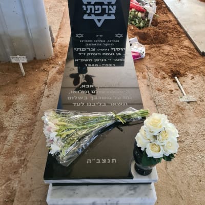 מצבה שחורה עם כיתוב בעברית ופרחים לבנים