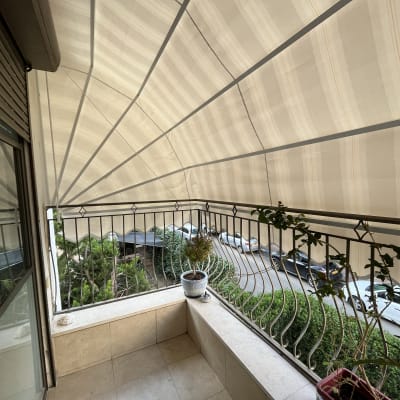 סוכך בד מתוח מעל מרפסת עם מעקה ברזל