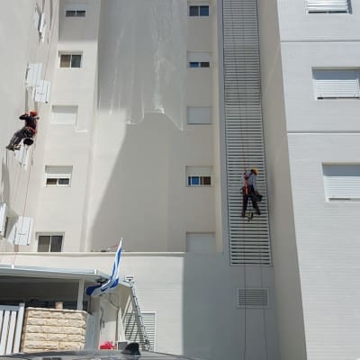 שני עובדים תלויים על חבלים על קיר בניין