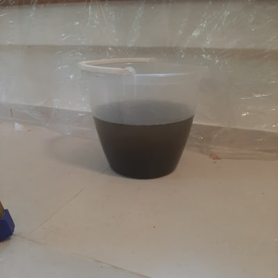 דלי עם מים כהים על רצפה ליד חלון