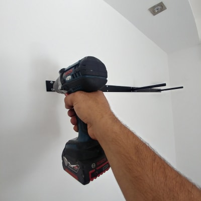 יד מחזיקה מברגה חשמלית על קיר לבן