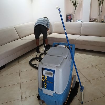 אדם מנקה ספה עם מכונת ניקוי מקצועית