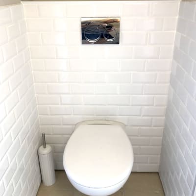 אסלה תלויה עם לחצן הדחה על קיר אריחים לבנים