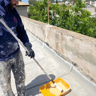 אדם מגלגל צבע על גג עם רולר ומגש צבע