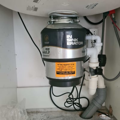 מכשיר טוחן אשפה מותקן מתחת לכיור עם צינורות חיבור