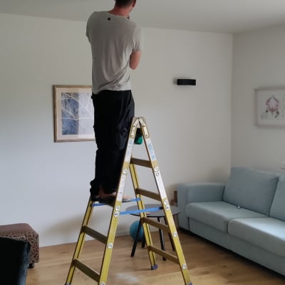 חשמלאי עומד על סולם ומתקין תאורה בתקרה