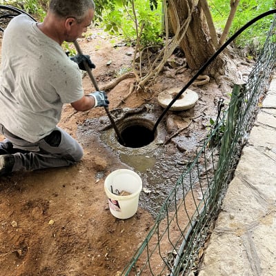 אדם מנקה בור עם צינור ליד עץ
