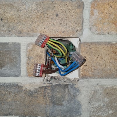 חוטי חשמל צבעוניים מחוברים לקופסת חיבורים בקיר