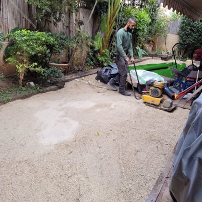 אדם עובד בגינה עם מכבש על משטח חול