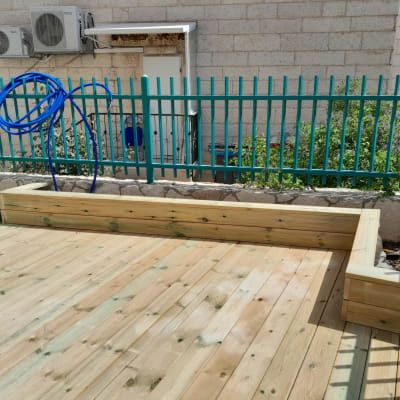 דק עץ עם אדנית צמודה וגדר מתכת ירוקה