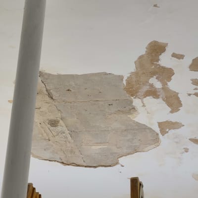 תקרה מתקלפת עם סימני תיקון ועמוד צבוע לבן