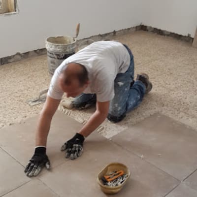 אדם מתקין אריחי רצפה עם דבק וכלים