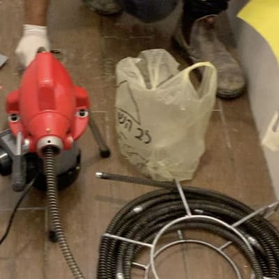 אדם עם כפפות ליד מכונת ניקוי צינורות אדומה