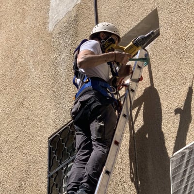 אדם על סולם עם מקדחה ליד פתח קיר