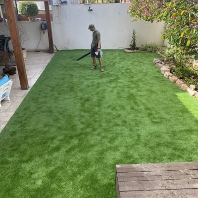 אדם משתמש במפוח על דשא סינתטי בגינה