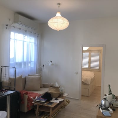 חדר עם ספה, שולחן קטן, מנורה עומדת, חלון עם וילון לבן