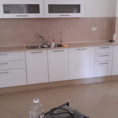 מטבח עם ארונות לבנים, כיור וברז, בקבוק ניקוי