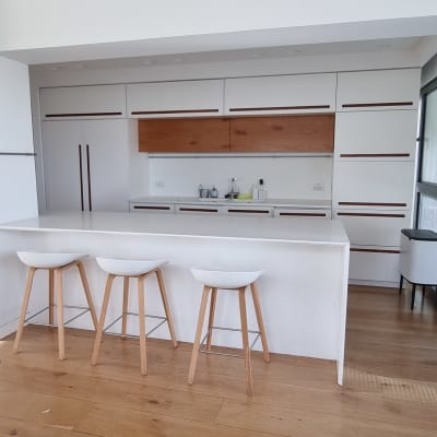 מטבח מודרני עם דלפק לבן ושלושה כיסאות עץ