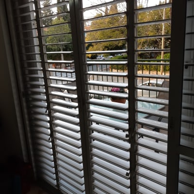 תריסים לבנים על חלון זכוכית עם נוף חיצוני