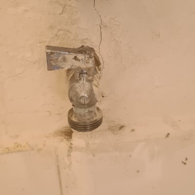 ברז מים ישן עם נזילה בקיר לבן