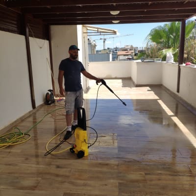 אדם משתמש במכונת שטיפה בלחץ על רצפת מרפסת