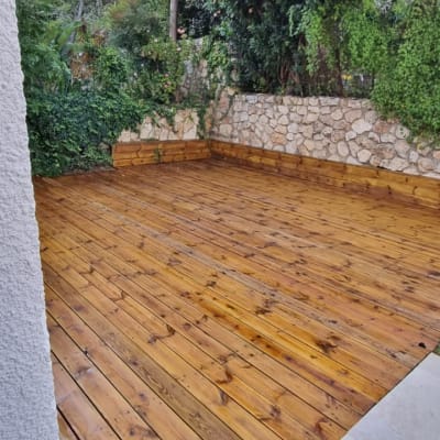 דק עץ בגינה עם קיר אבן וצמחייה ירוקה