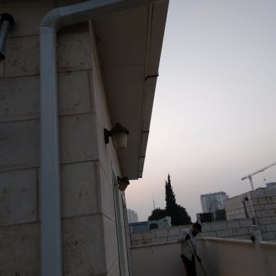 מרזב לבן מחובר לגג בניין אבן