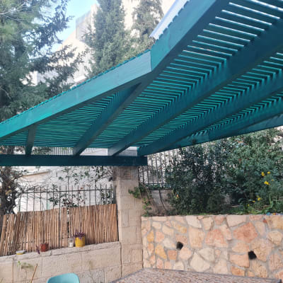 פרגולה מעץ צבועה בירוק בגינה עם צמחים