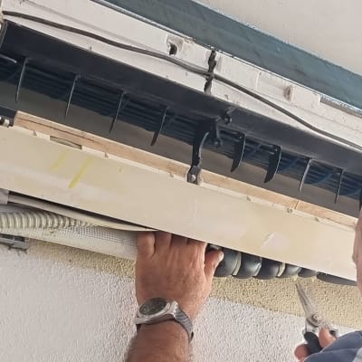 אדם מתקן מזגן עם כלי עבודה בידו