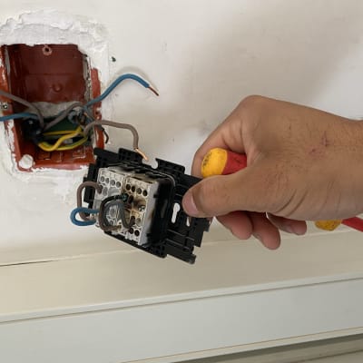 יד מחזיקה כלי עבודה ליד חוטי חשמל בקיר