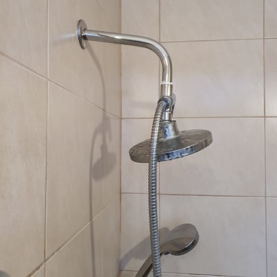 ראש מקלחת מתכת עם צינור גמיש על קיר אריחים