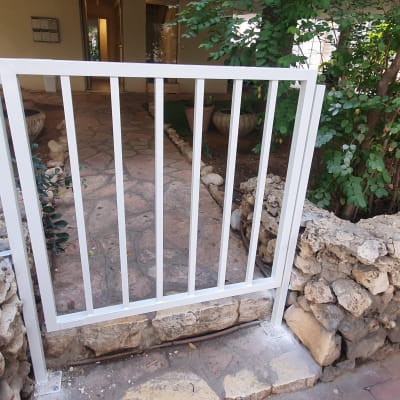 שער מתכת לבן בין קירות אבן בגינה